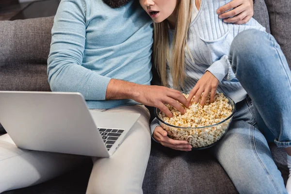 Croped view of couple sitting on sofa and watching movie on laptop — Stock Photo