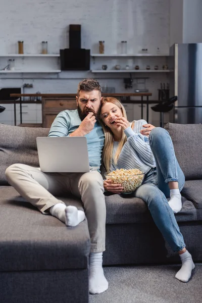 Husband and wife sitting on sofa and watching movie on laptop — Stock Photo