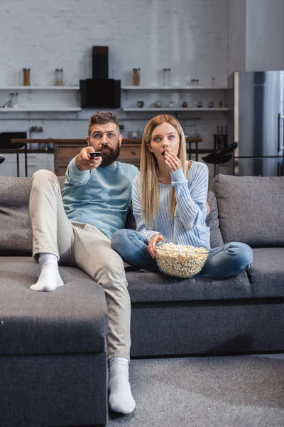 Pareja sentada en un sofá con palomitas de maíz y viendo películas - foto de stock