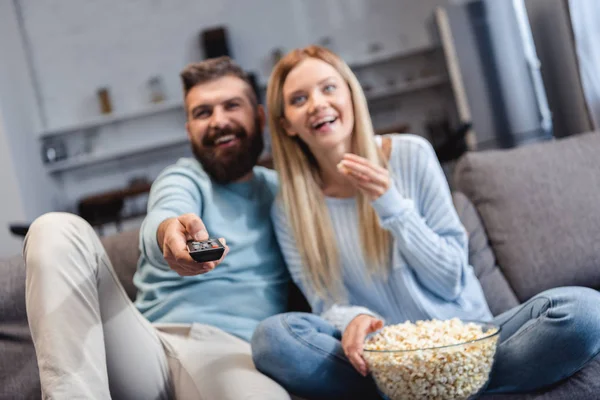 Happy couple sitting on sofa with popcorn and watching movie — Stock Photo