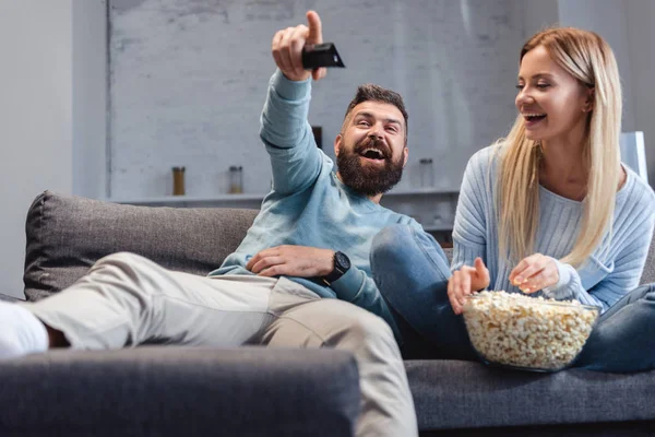 Husband and wife laughing and sitting on sofa with popcorn — Stock Photo