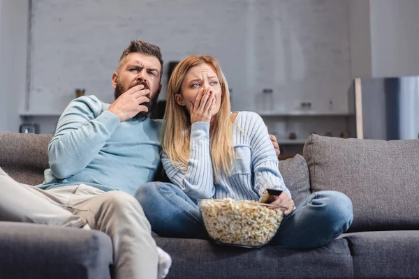 Sleepy couple sitting on sofa with popcorn — Stock Photo