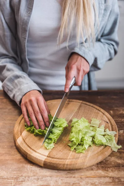 Vista ritagliata della donna che taglia foglie di insalata verde in cucina — Foto stock