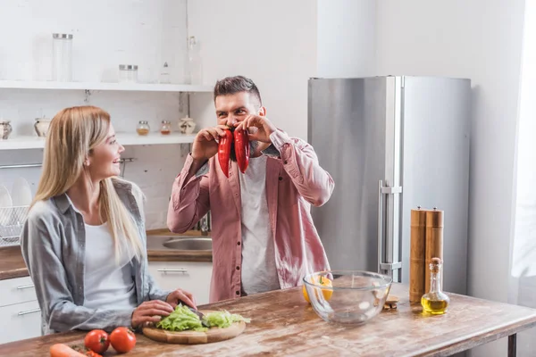 Fröhlicher Ehemann spielt mit Gemüse in der Nähe seiner Frau — Stockfoto