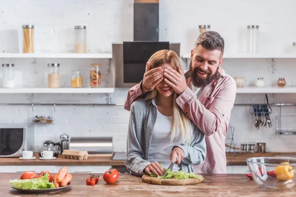 Husband smiling and closing eyes of wife in kitchen — Stock Photo