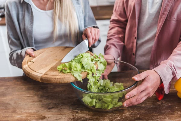 Vista ritagliata della donna che aggiunge foglie di insalata e ciotola uomo — Foto stock