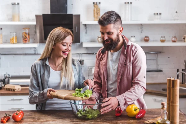 Fröhliches Paar gibt Salatblätter in Schüssel — Stockfoto