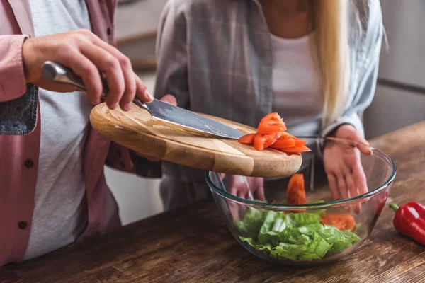 Vista recortada del hombre añadiendo tomates en ensalada y mujer sosteniendo tazón - foto de stock