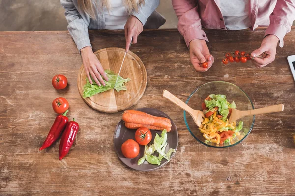 Vista recortada de pareja cocinar ensalada de verduras juntos en la mesa de madera - foto de stock