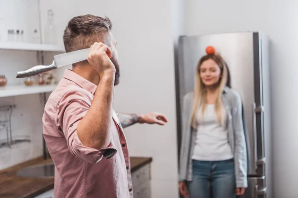 Homme jetant couteau pointu à la tomate sur la tête de la femme tout en jouant jeu dangereux — Photo de stock