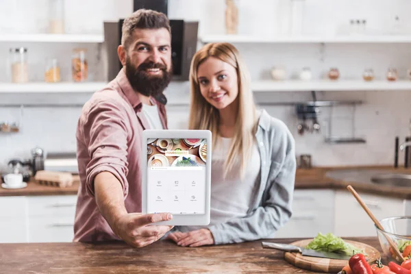 Couple holding digital tablet with foursquare app on screen at kitchen — Stock Photo