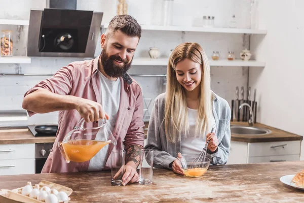 Pareja joven preparando el desayuno juntos en la cocina y beber jugo - foto de stock