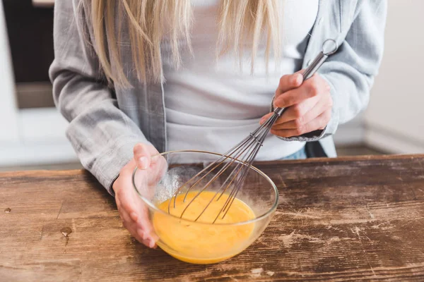 Cropped view of woman whipping eggs in glass bowl at wooden table — Stock Photo