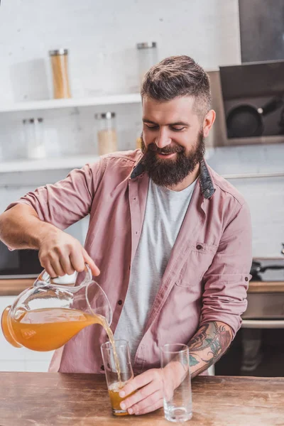 Homem sorridente derramando suco de jarra em copos à mesa de madeira — Fotografia de Stock