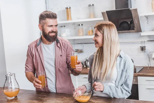 Young woman preparing breakfast while cheerful man holding glasses with juice — Stock Photo