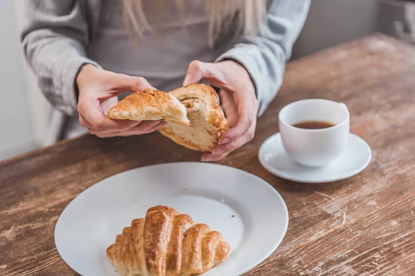 Vista ritagliata delle mani femminili che tengono il croissant al tavolo di legno — Foto stock
