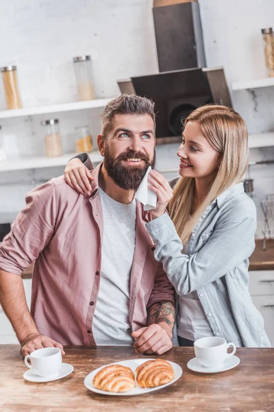 Mulher carinhosa limpando barba homem com guardanapo na cozinha — Fotografia de Stock