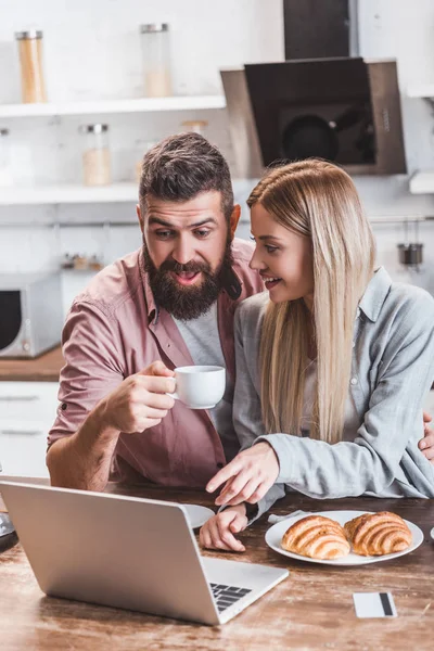 Приваблива жінка вказує на екран ноутбука, а щасливий чоловік п'є каву — стокове фото