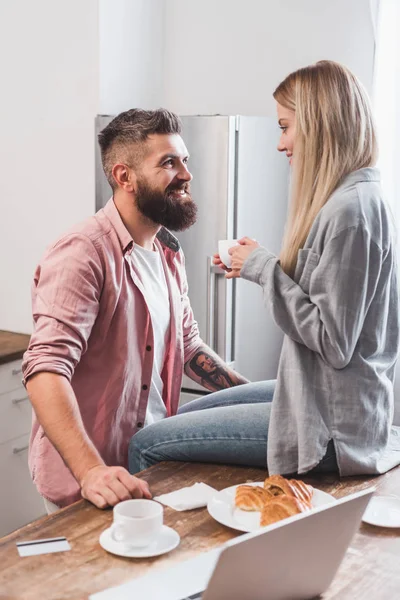 Sorrindo casal tomando café da manhã e fazendo compras on-line na cozinha — Fotografia de Stock