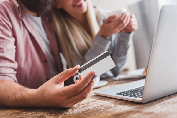 Cropped view of man holding credit card while smiling woman drinking coffee — Stock Photo