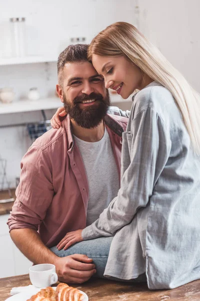 Attraente giovane donna che abbraccia sorridente uomo barbuto in cucina — Foto stock