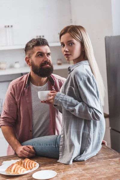 Beautiful woman sitting on wooden table with coffee cup and croissants while man looking at girl — Stock Photo
