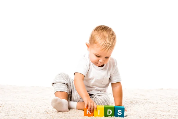 Cute toddler boy playing colored cubes with letters on carpet isolated on white — Stock Photo