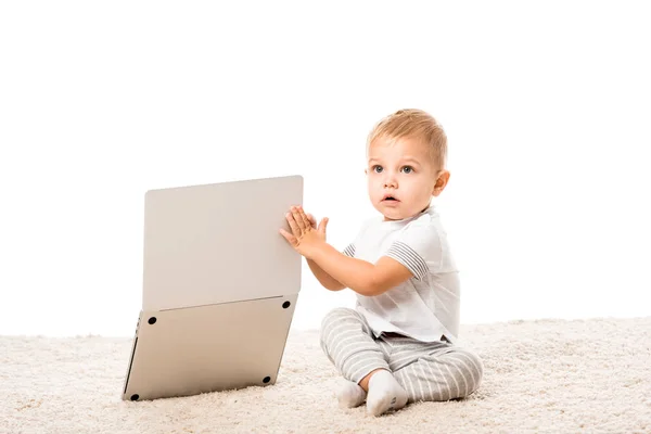Mignon tout-petit garçon assis sur le tapis et tenant ordinateur portable isolé sur blanc — Photo de stock