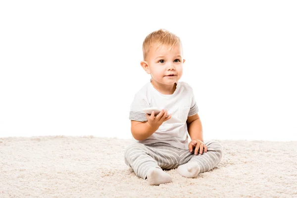 Adorable toddler boy with smartphone sitting on carpet isolated on white — Stock Photo