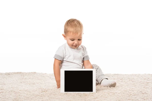 Niño sonriente con tableta digital sentado en la alfombra aislado en blanco - foto de stock
