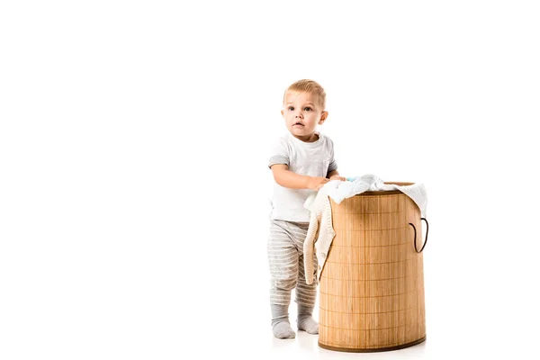 Nice toddler boy standing near wicker laundry basket isolated on white — Stock Photo