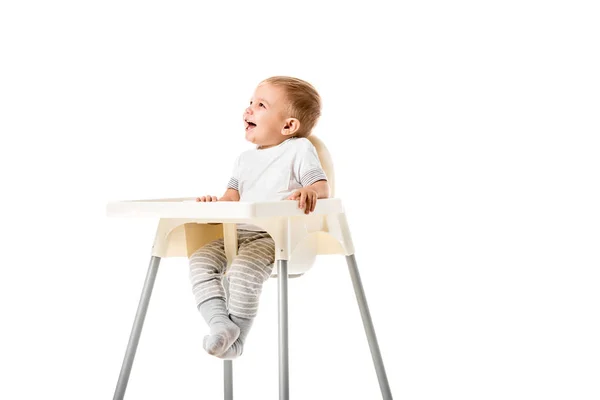 Niño feliz sonriendo y sentado en silla alta aislado en blanco - foto de stock