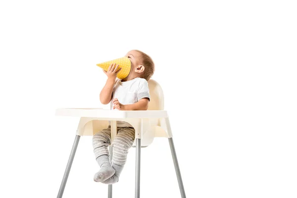 Bambino ragazzo tenendo giallo cappello partito e seduto in seggiolone isolato su bianco — Foto stock