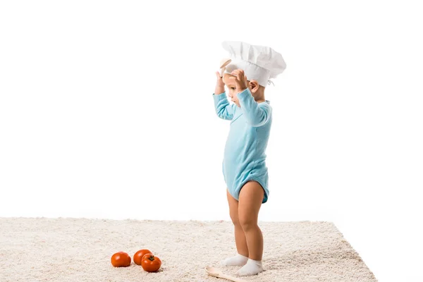 Bambino ragazzo in cuochi cappello in piedi vicino pomodori freschi su tappeto isolato su bianco — Foto stock