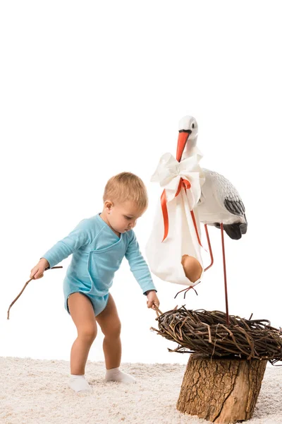 Toddler boy pulling out sticks from decorative stork nest isolated on white — Stock Photo