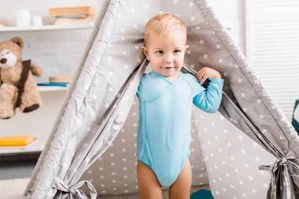 Cute toddler boy in blue bodysuit standing in baby wigwam — Stock Photo