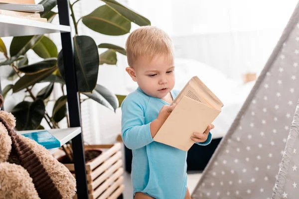 Carino bambino ragazzo in body blu che tiene libro in camera da letto — Foto stock