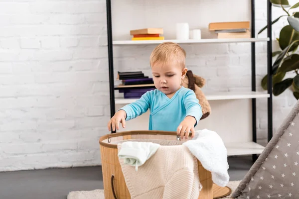 Carino bambino in body blu in piedi vicino a vimini cesto lavanderia in camera — Foto stock