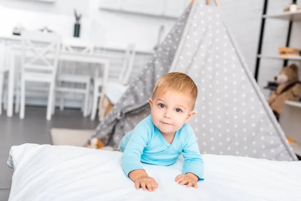 Cute toddler boy standing near bed, smiling and looking at camera in apartment — Stock Photo