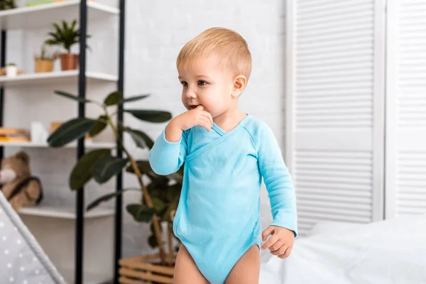 Adorable bébé mettre le doigt dans la bouche et debout sur le lit dans la chambre d'enfant — Photo de stock