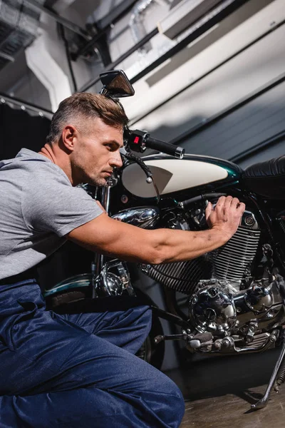 Handsome adult mechanic fixing motorcycle engine in garage — Stock Photo