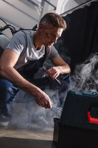 Mechanic holding wrenches next to motorbike in garage — Stock Photo