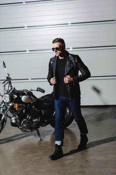 Cool guy in sunglasses and leather jacket walking in garage — Stock Photo