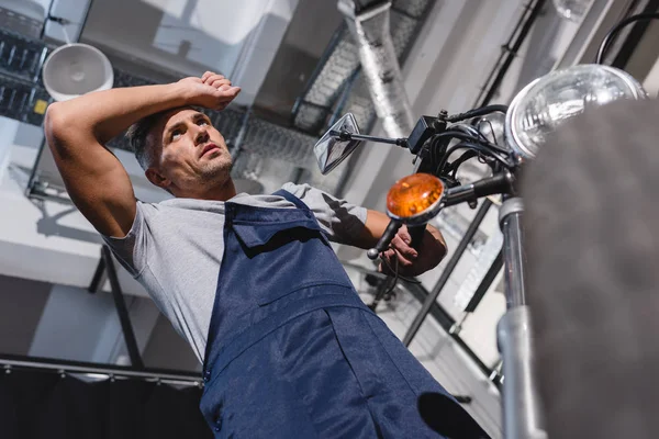 Adult mechanic wiping forehead after repairing motorcycle in garage — Stock Photo