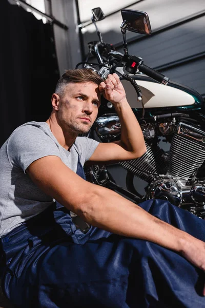 Mechanic with hand on forehead next to motorbike in garage — Stock Photo