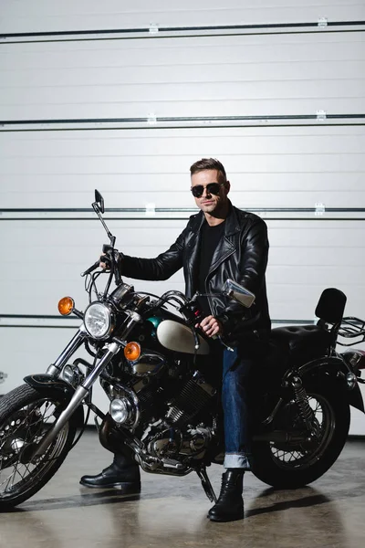 Homem bonito em óculos de sol sentado na motocicleta e olhando para a câmera — Fotografia de Stock
