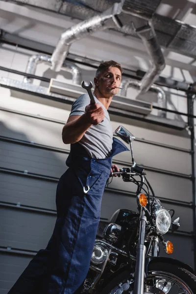 Mechanic with wrench in hand next to motorbike in garage — Stock Photo