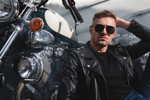 Handsome guy in sunglasses sitting by motorcycle in garage — Stock Photo