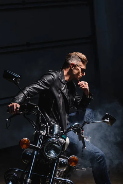 Classic biker in sunglasses sitting on motorbike in garage — Stock Photo