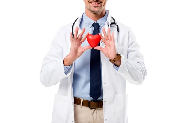 Vista parcial del médico sonriente en bata blanca con estetoscopio sosteniendo el modelo de corazón en manos aisladas en blanco, concepto de atención médica del corazón - foto de stock